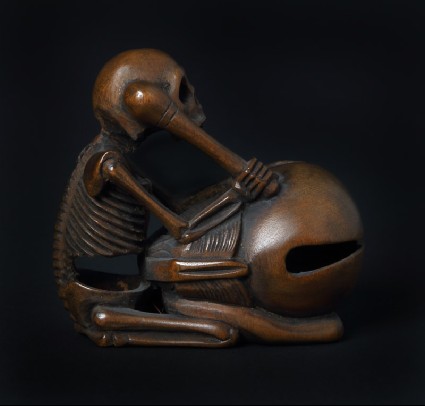 Netsuke in the form of a skeleton kneeling in front of a mokugyō, a Buddhist percussion instrumentfront