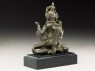 Seated figure of a crowned deity with four arms upon another figure (side)